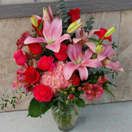 Bouquet of pink lilies, red roses, and pink hydrangea in a glass vase