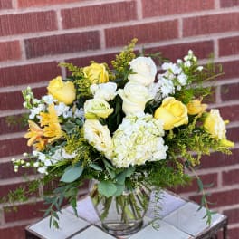 Yellow and white roses in a clear glass vase with mixed greenery