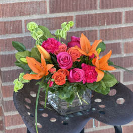 Bright bouquet of orange lilies and pink roses in a glass cube vase