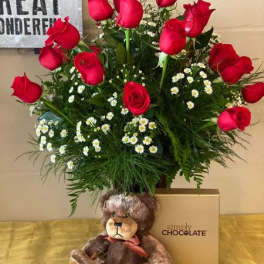 Red roses arranged with small white daisies, a teddy bear, and a chocolate box