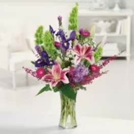 Mixed bouquet of pink lilies and purple flowers in a clear glass vase