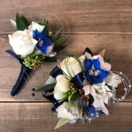 Two white and blue floral boutonnieres on a wooden surface