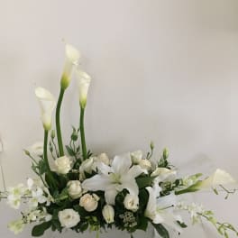 White floral arrangement with calla lilies, roses, and a lily in a rectangular vase