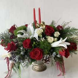 Red roses and white lilies arranged in a gold vase with two red candles