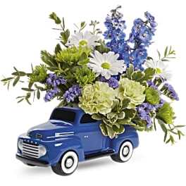 Blue truck-shaped planter filled with white, blue, and green flowers
