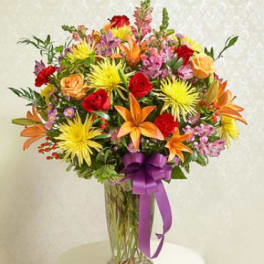 Colorful mixed bouquet in a clear glass vase with a purple ribbon