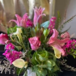 Pink lilies, roses, and pale calla lilies arranged with bright filler flowers in a white vase