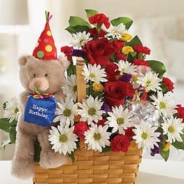 Teddy bear beside a basket of red and white flowers with a birthday hat