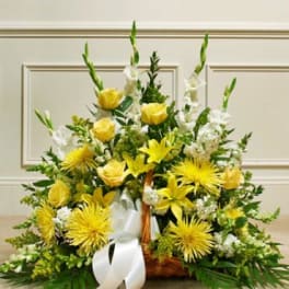 Yellow and white floral arrangement in a wicker basket with a white ribbon
