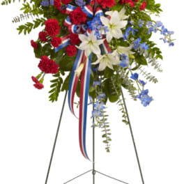 Standing floral spray with red carnations, white lilies, and blue accents