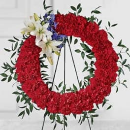 Red floral wreath on a stand with white lilies and blue accents