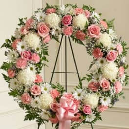 Pink and white floral wreath on a black stand with a pink ribbon