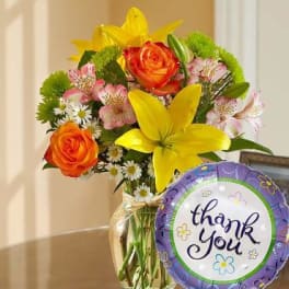 Bouquet of orange roses and yellow lilies in a glass vase with a thank-you balloon