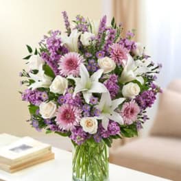 Bouquet of white lilies, pink daisies, and purple flowers in a glass vase