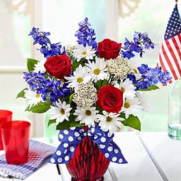 Red roses and white daisies in a red vase with a blue polka-dot bow