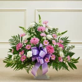 Pink and white floral arrangement with a purple ribbon on a stand