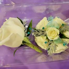Two cream rose corsages in a purple plastic box