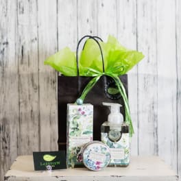 Gift bag with floral-patterned soap and lotion bottles and a small tin
