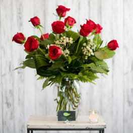 Red roses arranged in a clear glass vase with small white filler flowers.