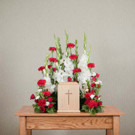 Red and white floral arrangement around a wooden cross urn.