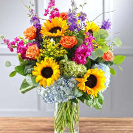 Mixed bouquet with sunflowers, roses, and hydrangeas in a glass vase