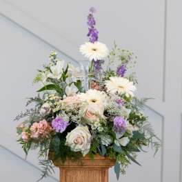 Mixed pastel flower arrangement in a clear glass vase on a wooden pedestal