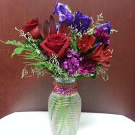 Mixed bouquet of red, purple, and blue flowers in a glass vase