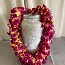 Purple and yellow orchid lei draped over a silver vase