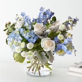 Arrangement of white roses, blue delphinium and hydrangea in a clear glass vase