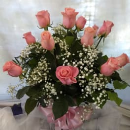 Pink roses arranged in a bouquet with baby's breath and a pink ribbon