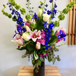 Tall mixed bouquet with pink lilies, blue delphinium, and white roses in a black vase