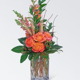 Orange roses in a clear glass vase with tall pink blooms