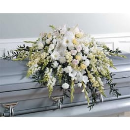 White floral casket spray with trailing greenery on a gray casket
