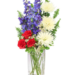 Red roses, purple flowers, and white blooms in a clear rectangular vase