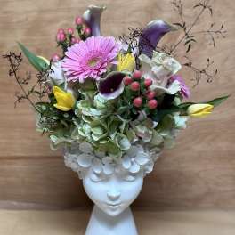 Floral arrangement in a white face-shaped vase with pink and yellow blooms