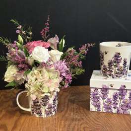 Pink and white flower arrangement in a lavender bee-patterned mug beside a matching mug and box