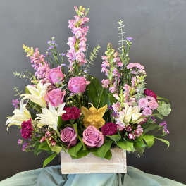 Pink roses and lilies arranged in a wooden box with a small angel figurine.