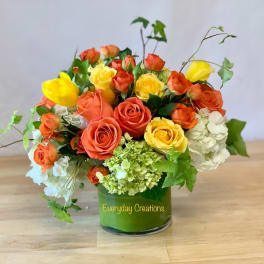Orange and yellow roses with white hydrangeas in a glass vase