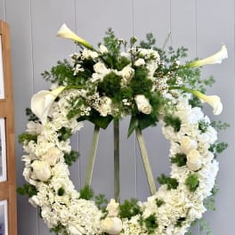 White floral wreath on an easel with calla lilies and roses