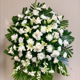 Large standing spray of white roses, lilies, and mums with bold green foliage