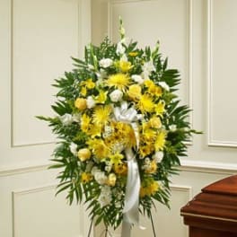 Yellow and white funeral spray on a stand with a white ribbon