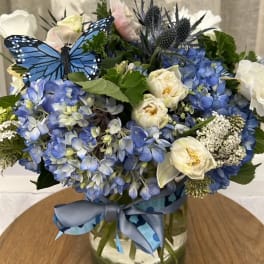 Blue and white flower arrangement in a glass vase with a ribbon and butterfly decoration