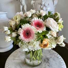 Bouquet of pink gerbera daisies, white roses, and pale hydrangeas in a glass vase