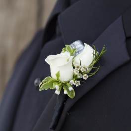 White rose boutonniere pinned to a dark suit jacket