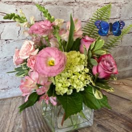 Pink mixed bouquet with green hydrangea and a blue butterfly pick in a clear glass cube vase