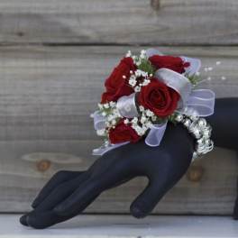 Red rose wrist corsage with white filler flowers and silver ribbon on a black display hand