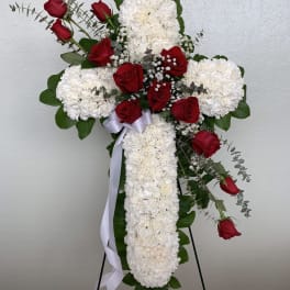 Cross-shaped floral tribute with red roses and white carnations on a stand