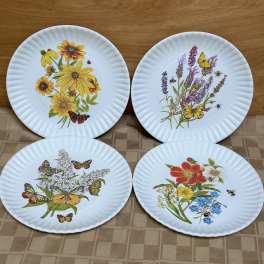 Four white plates with colorful floral and butterfly designs