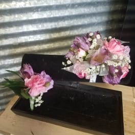Pink and purple floral corsage and boutonniere set on black display stands