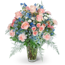 Pink roses, blue flowers, and white blooms in a clear glass vase